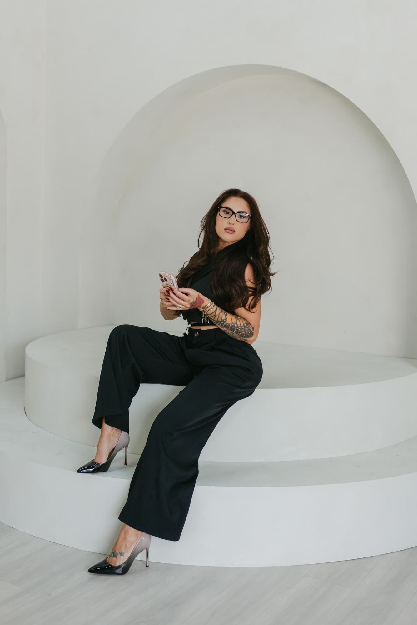 Meagan Greene seated on a curved white studio plinth holding her phone